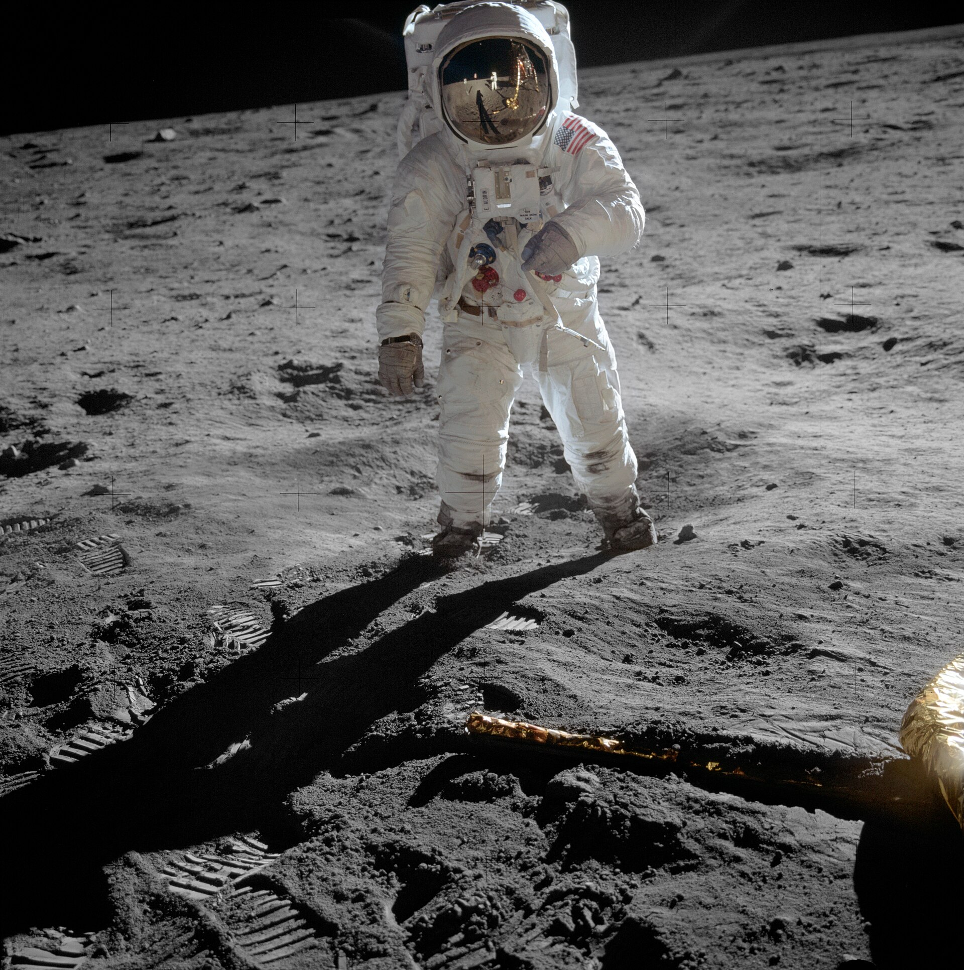 Buzz Aldrin stojący na Księżycu, w jego szybce hełmu odbijają się Neil Armstrong i lądownik