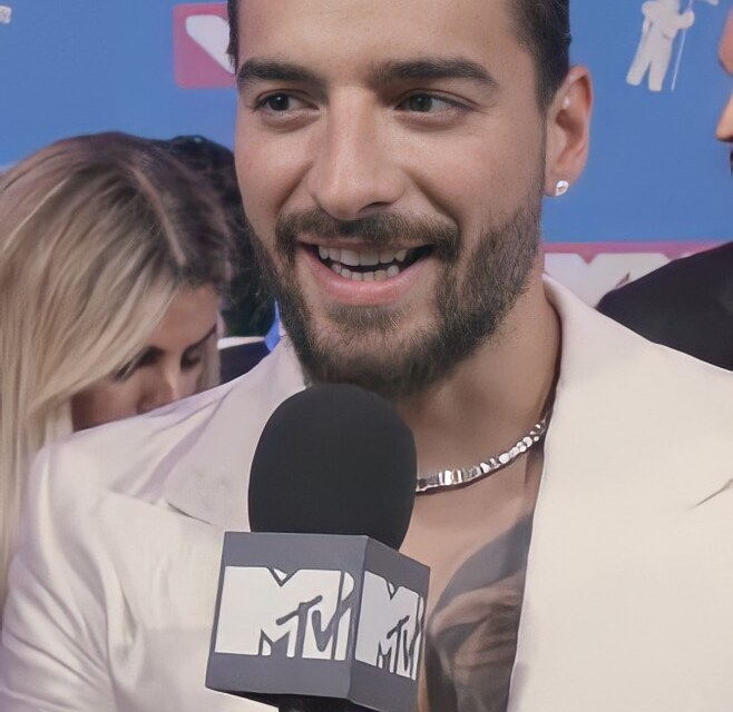 Uśmiechnięty Maluma w białym garniturze, z mikrofonem MTV