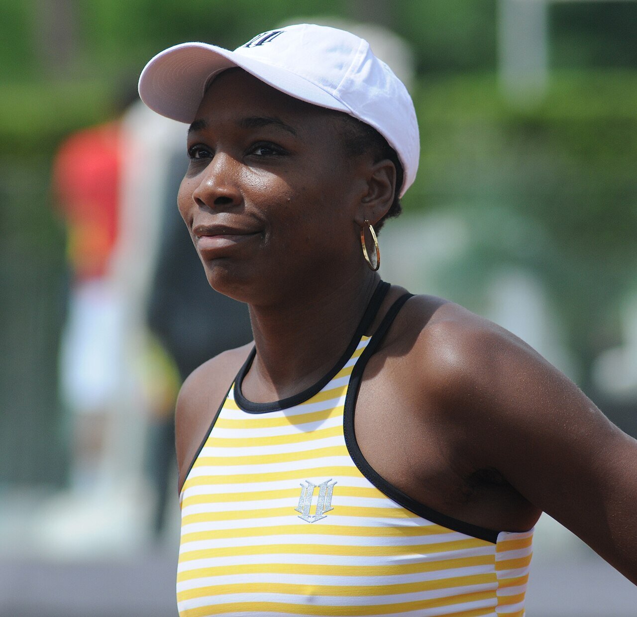 Venus Williams w białej czapce i bluzce w żółto-białe paski; na piersi i na czapce logo w kształcie litery V z dwóch jedynek